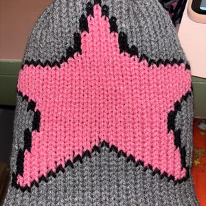 May include: Grey knitted beanie with a pink star outlined in black.