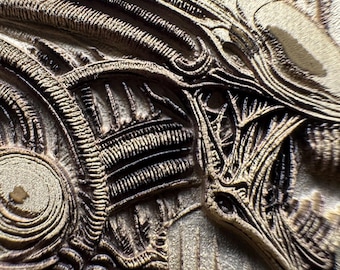 May include: Close-up of a detailed, textured relief sculpture depicting the head of an alien creature. The sculpture features intricate patterns and a mix of light and dark brown tones, creating a three-dimensional effect. The design is reminiscent of science fiction.