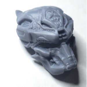 May include: A detailed, gray, 3D-printed model of a stylized creature skull. The skull features intricate details, including sharp teeth and textured surfaces. The model is set against a white background.