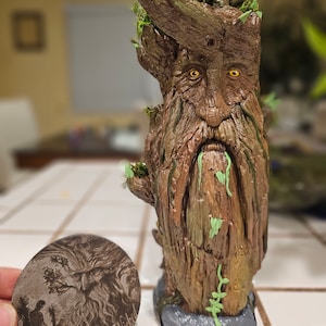 May include: A detailed, hand-painted tree-like sculpture with a face, beard, and moss accents. The sculpture has a weathered brown finish with green highlights. A wooden, oval-shaped item with the text "Painted Wicked" and a detailed illustration is next to the sculpture.