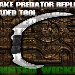 May include: A silver bladed tool with a curved design and a black handle. The text "SNAKE PREDATOR REPLICA BLADED TOOL" is at the top, and "PRINTED WICKED" is at the bottom. The background is a detailed, metallic, industrial design.