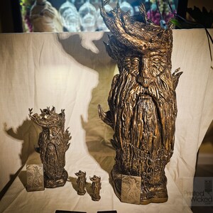 May include: Bronze-colored sculptures of a bearded, tree-like figure with a crown of leaves. The sculptures vary in size, with a large bust and smaller figurines. The figures have detailed textures and are displayed with small cards.
