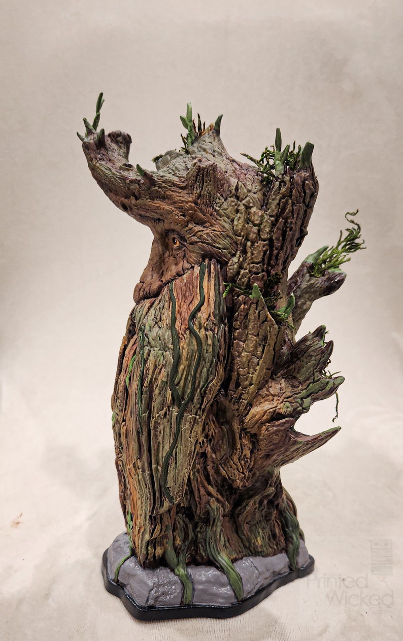 May include: A detailed sculpture of a tree-like figure with a textured, weathered appearance. The sculpture features shades of brown, green, and gray, with intricate details mimicking bark, moss, and foliage. The base is a gray stone-like structure.