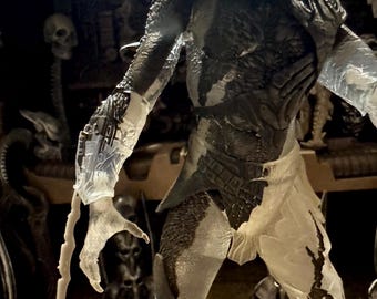 May include: A detailed action figure of a Predator, featuring a dark gray and translucent design. The figure has intricate armor, a helmet, and extended claws. The figure is posed in a dynamic stance, showcasing its detailed textures and design.