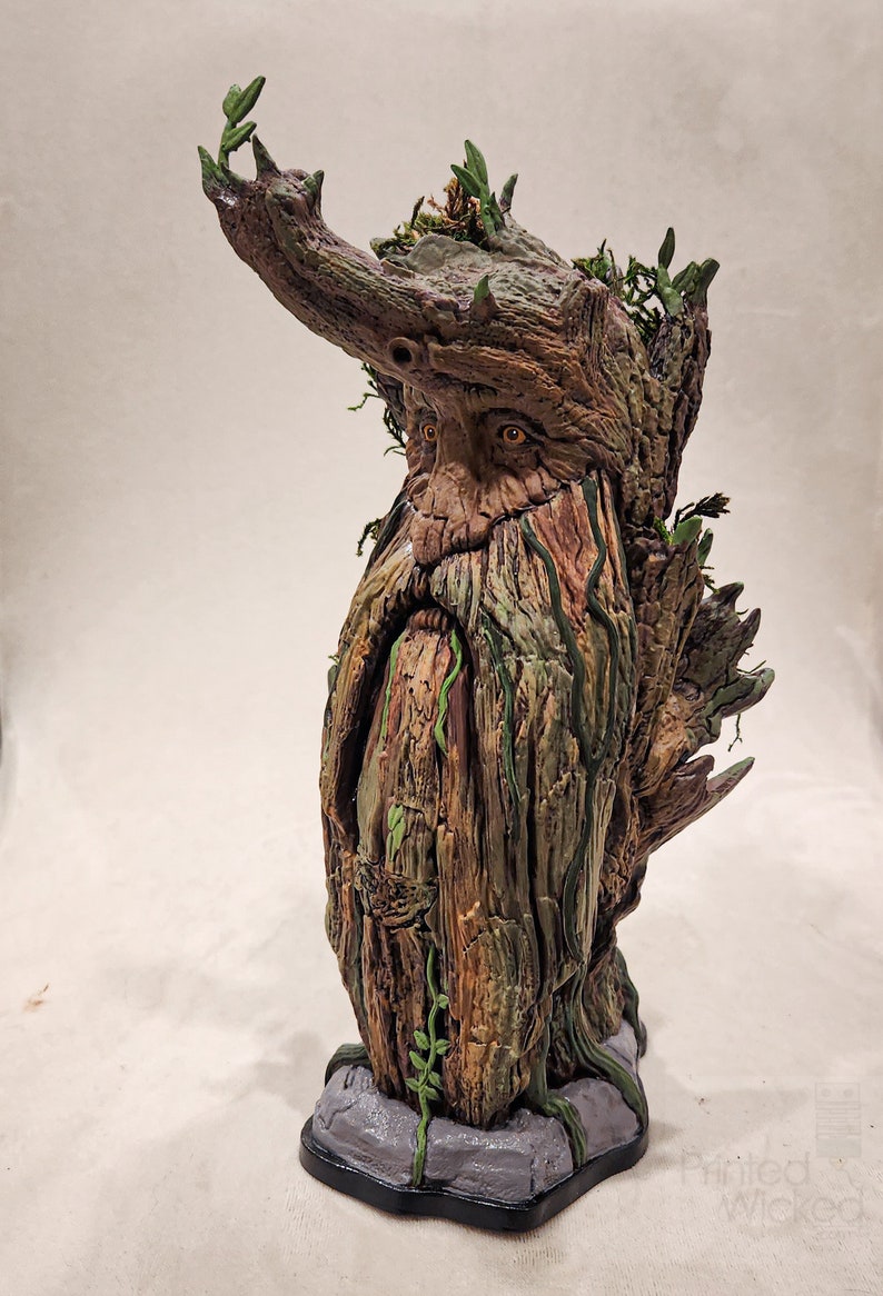 May include: A detailed sculpture of a tree-like figure with a long beard and leafy crown. The figure has a weathered, textured appearance with shades of brown, green, and gray. The base is a gray stone-like structure.