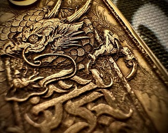 May include: Close-up of a detailed, gold-colored relief carving featuring a dragon. The dragon's head is prominent, with intricate scales and a detailed design. The carving includes stylized lettering and a textured background.