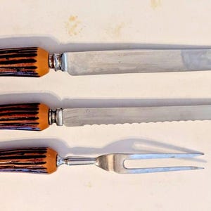 以下が含まれることがあります： 滑らかな刃のナイフ、波刃のパン切りナイフ、2本歯のカービングフォークの3点セット。各カトラリーは、ダークブラウンとタンのストライプ模様が施された湾曲した質感のあるハンドルと、シルバーメタルのボルスターが特徴です。