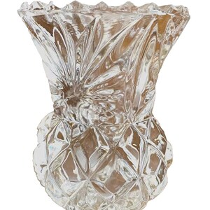 Può includere: Vaso di vetro trasparente con base a motivo diamantato e parte superiore svasata e scanalata. Il vaso ha la forma di un ananas ed è progettato per contenere fiori o altri oggetti decorativi. Il vetro è trasparente.