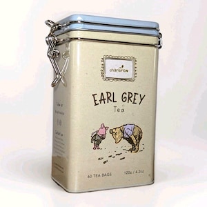 Puede incluir: Una lata de té rectangular de color blanquecino con tapa azul claro y cierre plateado. La lata presenta el texto "Earl Grey Tea" y una ilustración de dos osos de dibujos animados. También indica "60 bolsitas de té" y "120g / 4.2oz".