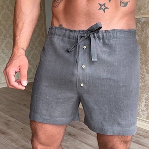 K&ouml;nnte beinhalten: Graue Leinenhose mit Kordelzugbund und Knopfverschluss. Die Hose hat eine lockere Passform und ist aus einem leichten Stoff gefertigt.
