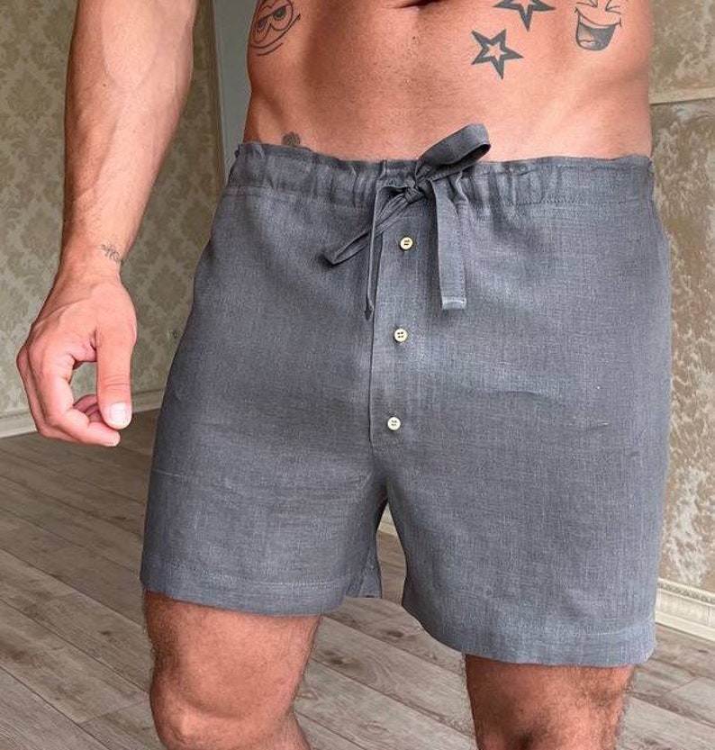 K&ouml;nnte beinhalten: Graue Leinenhose mit Kordelzugbund und Knopfverschluss. Die Hose hat eine lockere Passform und ist aus einem leichten Stoff gefertigt.