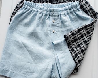 May include: Two pairs of shorts, one light blue and one black and white checked. The light blue shorts have a button fly and an elastic waistband.