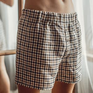 Op de afbeelding: Een paar bruine en zwarte geruite pyjamabroeken met een knoopsluiting.