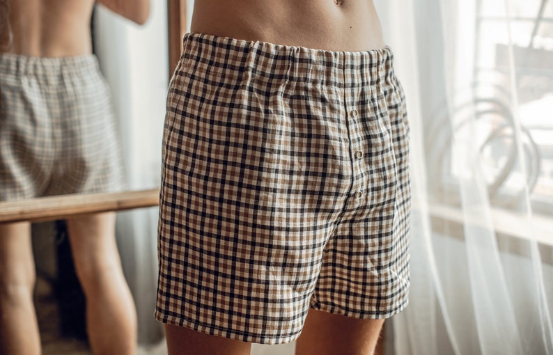 Op de afbeelding: Een paar bruine en zwarte geruite pyjamabroeken met een knoopsluiting.