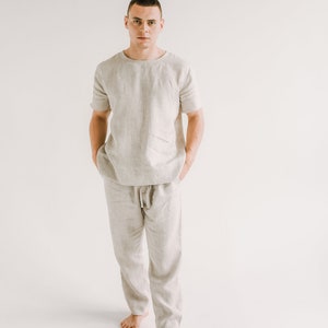 Op de afbeelding: Een persoon draagt een lichtbeige linnen shirt en broek. Het shirt heeft een ronde hals en korte mouwen. De broek heeft een trekkoord in de taille en een ontspannen pasvorm.