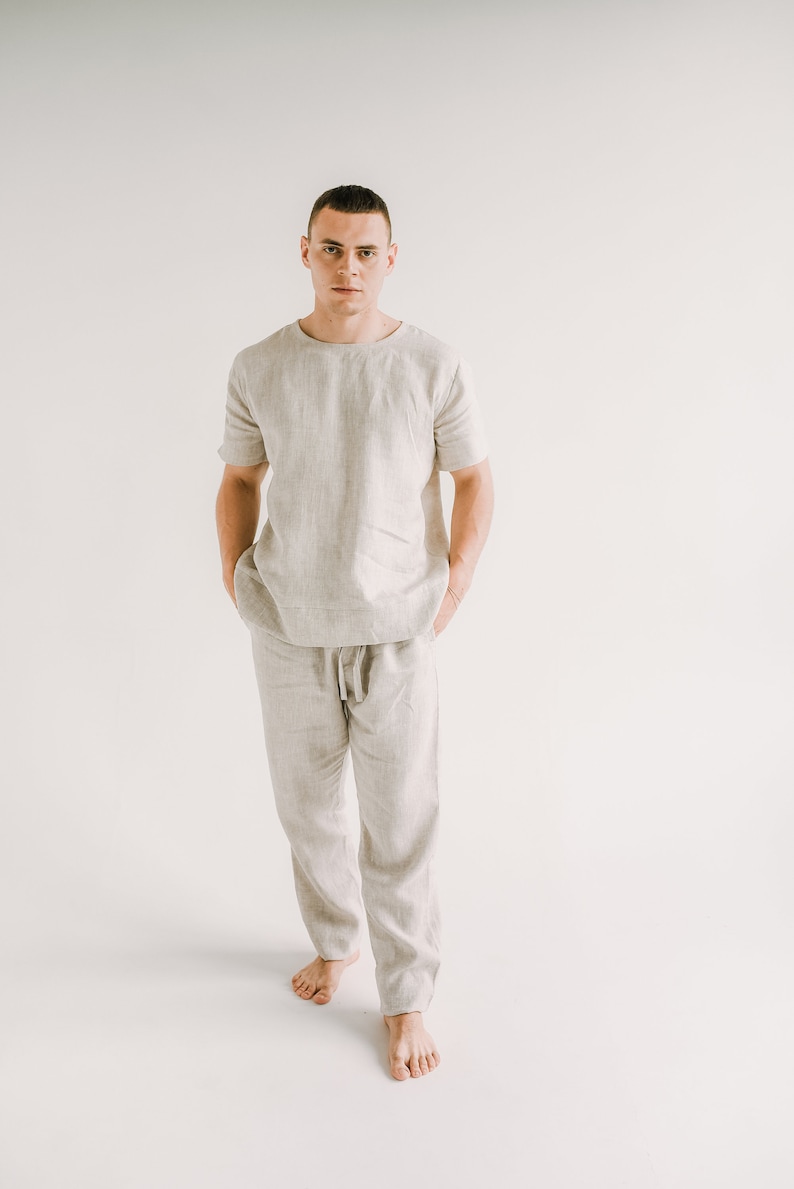 Op de afbeelding: Een persoon draagt een lichtbeige linnen shirt en broek. Het shirt heeft een ronde hals en korte mouwen. De broek heeft een trekkoord in de taille en een ontspannen pasvorm.