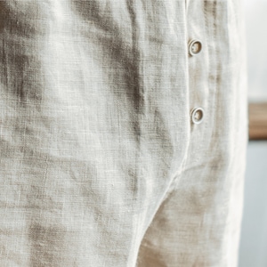 Op de afbeelding: Close-up van een paar beige linnen broek met een knoopsluiting.