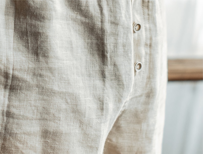 Op de afbeelding: Close-up van een paar beige linnen broek met een knoopsluiting.