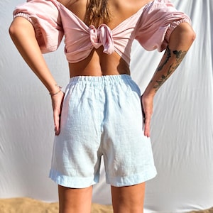 Pu&ograve; includere: Un top rosa chiaro con spalle scoperte, maniche a sbuffo e chiusura con fiocco sulla schiena, abbinato a pantaloncini azzurri con elastico in vita. L'insieme &egrave; ripreso di spalle, mettendo in risalto la consistenza del tessuto del top e dei pantaloncini.