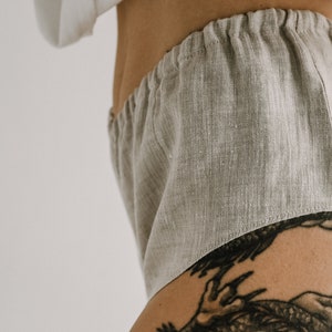 Pu&ograve; includere: Primo piano di pantaloncini in lino beige chiaro con elastico in vita. I pantaloncini sono realizzati in un tessuto strutturato e sembrano comodi. I pantaloncini fanno parte di un set loungewear.