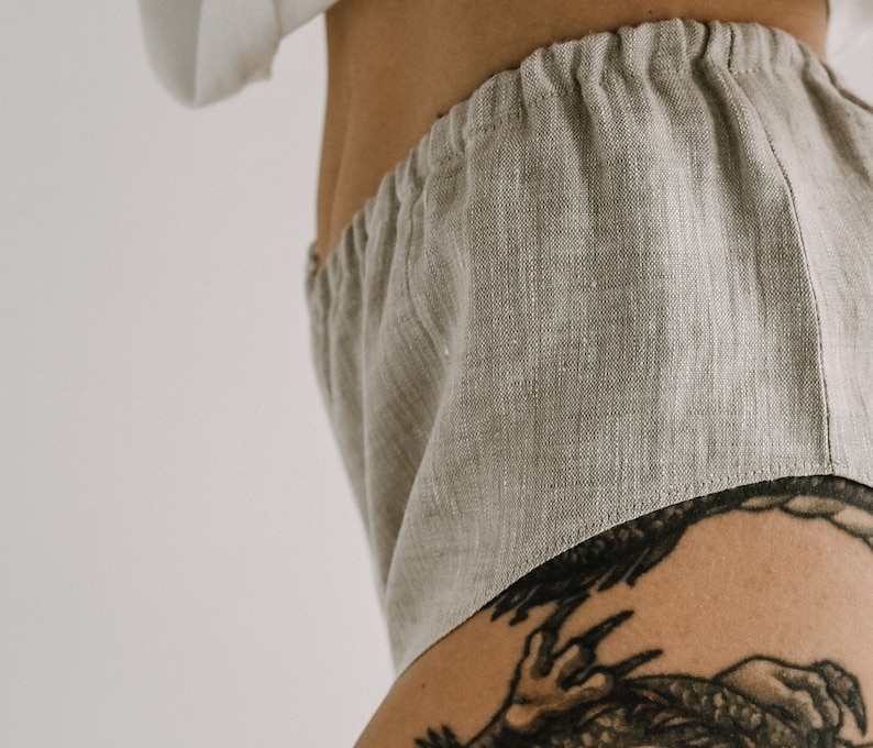 Pu&ograve; includere: Primo piano di pantaloncini in lino beige chiaro con elastico in vita. I pantaloncini sono realizzati in un tessuto strutturato e sembrano comodi. I pantaloncini fanno parte di un set loungewear.