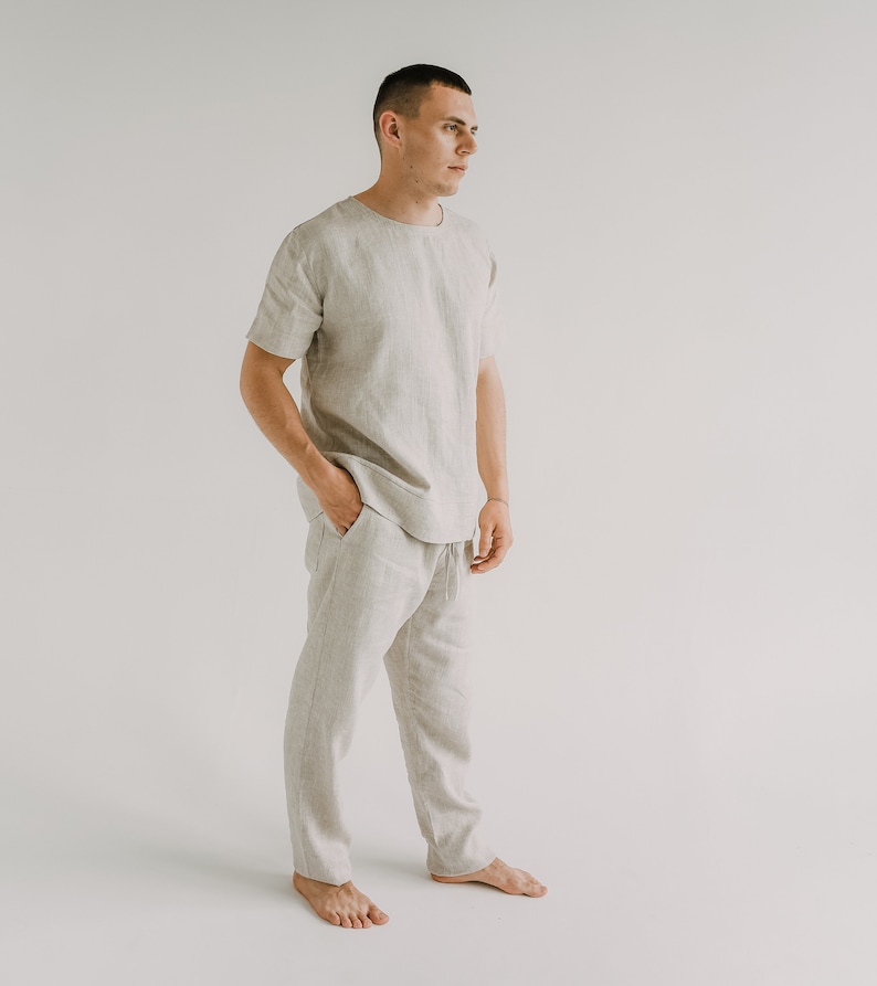 Op de afbeelding: Een persoon draagt een lichtbeige linnen shirt en een bijpassende broek. Het shirt heeft korte mouwen en een ronde hals. De broek heeft een trekkoord in de taille en is losjes gesneden.
