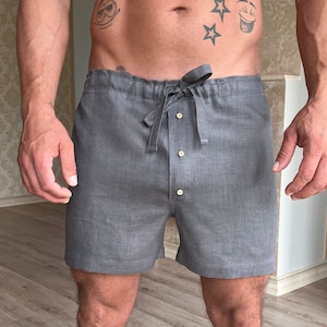 May include: Gray linen shorts with a drawstring waist and a button closure. The shorts have a relaxed fit and are made of a lightweight fabric.