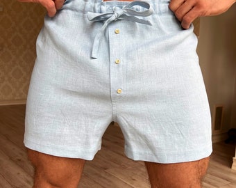 May include: Light blue linen shorts with a drawstring waist and button fastening. The shorts have a relaxed fit and are ideal for lounging around the house.