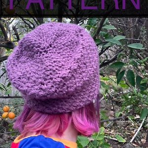 Op de afbeelding: Een paarse gebreide beanie met een textuurpatroon. De beanie wordt gedragen door een persoon met roze haar.