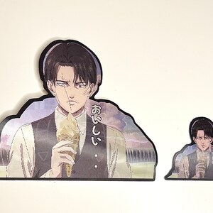 以下が含まれることがあります： アイスクリームを食べている黒髪男性のアニメキャラクターのステッカー2枚。大きい方のステッカーには「おいしい」という日本語が書かれています。