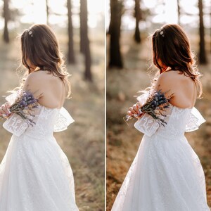 May include: A white off-the-shoulder dress featuring intricate lace detailing, short flared sleeves, and a full skirt. The garment is paired with a small bouquet of dried purple lavender flowers held against the back of the bodice.