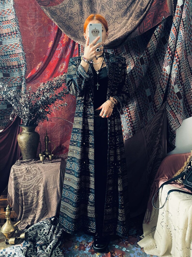 Puede incluir: Un vestido maxi largo con estampado negro y dorado con botones en la parte delantera. El vestido tiene un corte holgado y una silueta fluida.