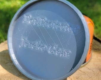 May include: A grey Pot Protector lid with the text "Pot Protector" and "Jereko Gear" printed on it. The lid is covering an orange container. The image is taken outdoors on a wooden surface.