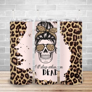 May include: A pink and brown tumbler with a leopard print design. The tumbler features a skull with a messy bun and sunglasses. The text "I'll sleep when I'm DEAD" is printed on the tumbler.