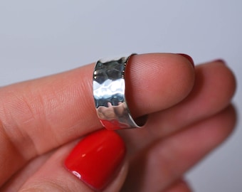 May include: A silver hammered ring with a wide band. The ring is worn on a finger with red nail polish.
