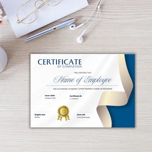 Op de afbeelding: Een certificaat van voltooiing met een gouden zegel en blauwe en gouden accenten. Het certificaat bevat de tekst "Certificaat van Voltooiing" en "Naam van de Werknemer". Een pen, bril en koptelefoon liggen op het houten oppervlak.