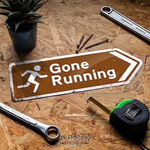 May include: A brown and white signpost with the words "Gone Running" and a running figure. Tools, including a wrench, tape measure, screws, and a small potted plant, surround the sign. The sign is on a wood grain surface.