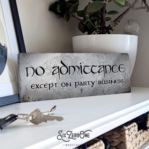 May include: A metal sign with a distressed, gray finish. The sign reads "no admittance except on party business" in a black, stylized font.
