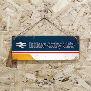 May include: A blue and white metal sign with the text "Inter-City 125" and a stylised train logo. The sign has a red, white and yellow stripe at the bottom.