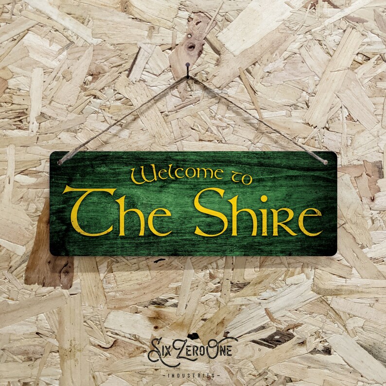 May include: A wooden sign with green paint and a yellow inscription that reads "Welcome to The Shire".
