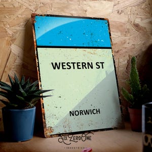 May include: A vintage-style metal sign with a blue and green colour scheme. The sign reads "WESTERN ST NORWICH".
