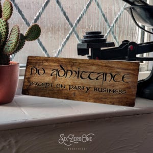 May include: A wooden sign with the text "no admittance except on party business" in a decorative font. The sign is brown with a wood grain texture.