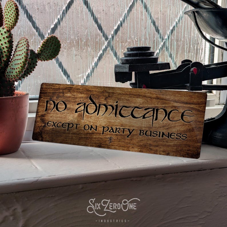 May include: A wooden sign with the text "no admittance except on party business" in a decorative font. The sign is brown with a wood grain texture.