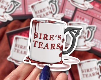Puede incluir: Una taza de café blanca con un asa negra y un diseño rojo que gotea. La taza dice "Sire's Tears" en letras rojas.