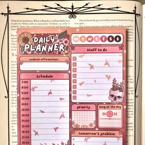 Pode incluir: Um autocolante de planeador diário rosa e pêssego com um design floral e de caveira. O planeador inclui secções para agendamento, listas de tarefas e acompanhamento da hidratação. O texto inclui "Daily Planner" e "Stay Hydrated!"