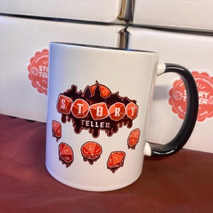 Peut inclure: Mug en c&eacute;ramique blanche avec une anse et un bord noirs. Le mug pr&eacute;sente les mots "STORY TELLER" dans une police rouge stylis&eacute;e avec un effet de sang d&eacute;goulinant et des illustrations de d&eacute;s rouges. Le mug est pour les amateurs de jeux de soci&eacute;t&eacute;.
