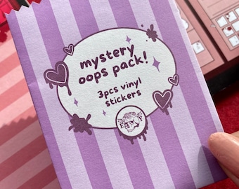 May include: A purple and white striped paper bag labeled "mystery oops pack!" with a heart and splatter design. The bag contains 3 vinyl stickers and features a skull logo.