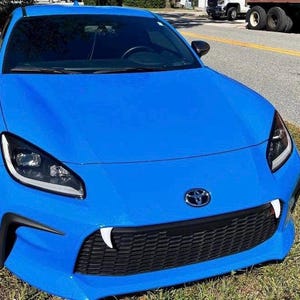 May include: A bright blue sports car with black accents and a black grille. The car has a black Toyota emblem on the front.