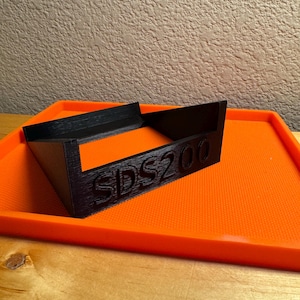 May include: A black plastic tray with the text "SDS200" printed on it. The tray is sitting on an orange tray.