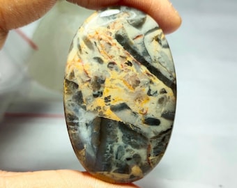 May include: A smooth, oval-shaped cabochon gemstone with a swirling pattern of grey, white, brown, and orange. The stone has a polished finish and is a natural agate.